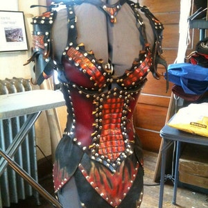 May include: A handcrafted leather bodice with a striking design. The armor features a combination of red, black, and orange leather, adorned with metal studs. The design includes a scale-like pattern and flame-like accents, creating a unique and detailed aesthetic.