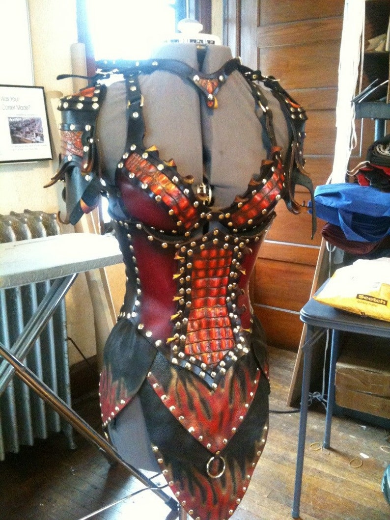May include: A handcrafted leather bodice with a striking design. The armor features a combination of red, black, and orange leather, adorned with metal studs. The design includes a scale-like pattern and flame-like accents, creating a unique and detailed aesthetic.