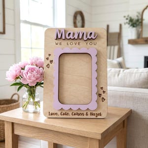 以下が含まれることがあります： 「Mama」の文字がラベンダー色の筆記体で書かれ、「WE LOVE YOU」というフレーズが入った木製のフォトフレーム。フレームはラベンダー色のスカラップボーダーで、「Love, Cole, Cohen & Hazel」の名前が含まれています。