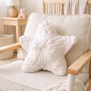 Puede incluir: Un coj&iacute;n blanco en forma de estrella, hecho de un material suave y texturizado. El coj&iacute;n est&aacute; colocado en un sill&oacute;n color crema con reposabrazos de madera. Una manta color crema est&aacute; sobre la silla. La habitaci&oacute;n tiene una paleta de colores neutros.