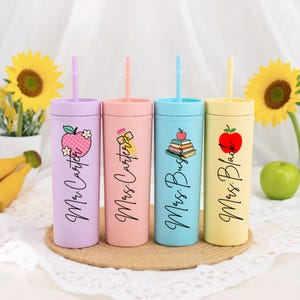 May include: Four colorful tumblers with straws, each featuring a different design and the name "Mrs. Carter" or "Mrs. Bush" or "Mrs. Black". The tumblers are pastel shades of purple, pink, blue, and yellow. Each tumbler has a different graphic, including an apple and books.