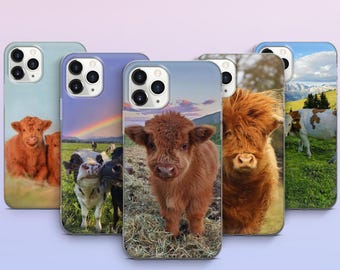 May include: A collection of phone cases featuring images of Highland cows. The cases display various scenes, including close-ups of the cows, a rainbow over a pasture, and a mountain landscape. The cases are in shades of blue, purple, and green.