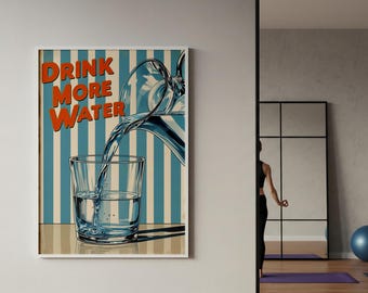 May include: A framed poster with the text "DRINK MORE WATER" in orange letters. The image depicts water being poured from a pitcher into a glass. The background has blue and white vertical stripes. The poster is in a white frame.