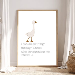 May include: A framed wall art print featuring a white goose with orange feet and a beak. Below the goose, the text reads: I can do all things through Christ who strengthens me. Philippians 4:13. The print is enclosed in a light wood frame.
