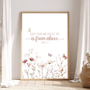 Può includere: Una stampa incorniciata con una cornice in legno chiaro. La stampa presenta un design floreale con fiori rosa e bianchi, farfalle e il testo "EVERY GOOD AND PERFECT GIFT is FROM ABOVE JAMES 1:7" in un carattere morbido ed elegante.