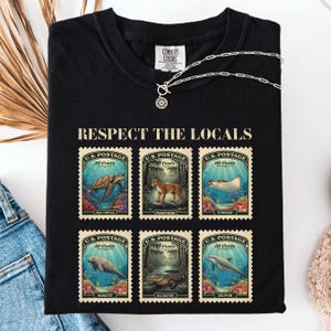 May include: Black t-shirt with the text "RESPECT THE LOCALS" above six postage stamp designs. Each stamp features a different marine animal: sea turtle, panther, stingray, manatee, alligator, and dolphin.