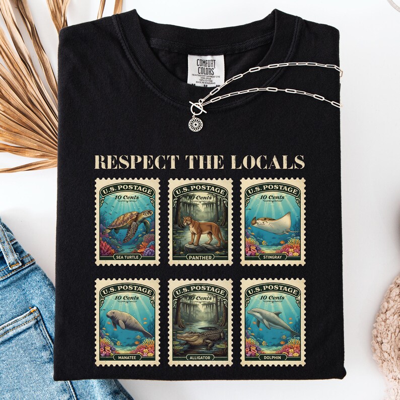 May include: Black t-shirt with the text "RESPECT THE LOCALS" above six postage stamp designs. Each stamp features a different marine animal: sea turtle, panther, stingray, manatee, alligator, and dolphin.