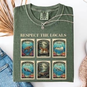 May include: Green Comfort Colors t-shirt with the text "RESPECT THE LOCALS" and six postage stamp designs featuring sea creatures. The stamps read "U.S. Postage 10 Cents" and depict a sea turtle, panther, stingray, manatee, alligator, and dolphin.