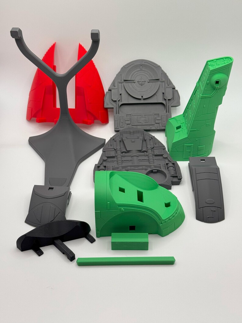 Puede incluir: Varias piezas de modelo impresas en 3D en rojo, gris, verde y negro. Los componentes, con formas geom&eacute;tricas y dise&ntilde;os detallados, parecen ser de un modelo m&aacute;s grande. Las piezas est&aacute;n dispuestas sobre una superficie blanca.