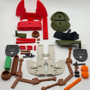 Puede incluir: Varias piezas de juguetes de pl&aacute;stico en rojo, verde, marr&oacute;n, gris y naranja. Las piezas incluyen espadas, escudos y otros componentes, probablemente para un juego de construcci&oacute;n. Las piezas est&aacute;n dispuestas sobre una superficie blanca.