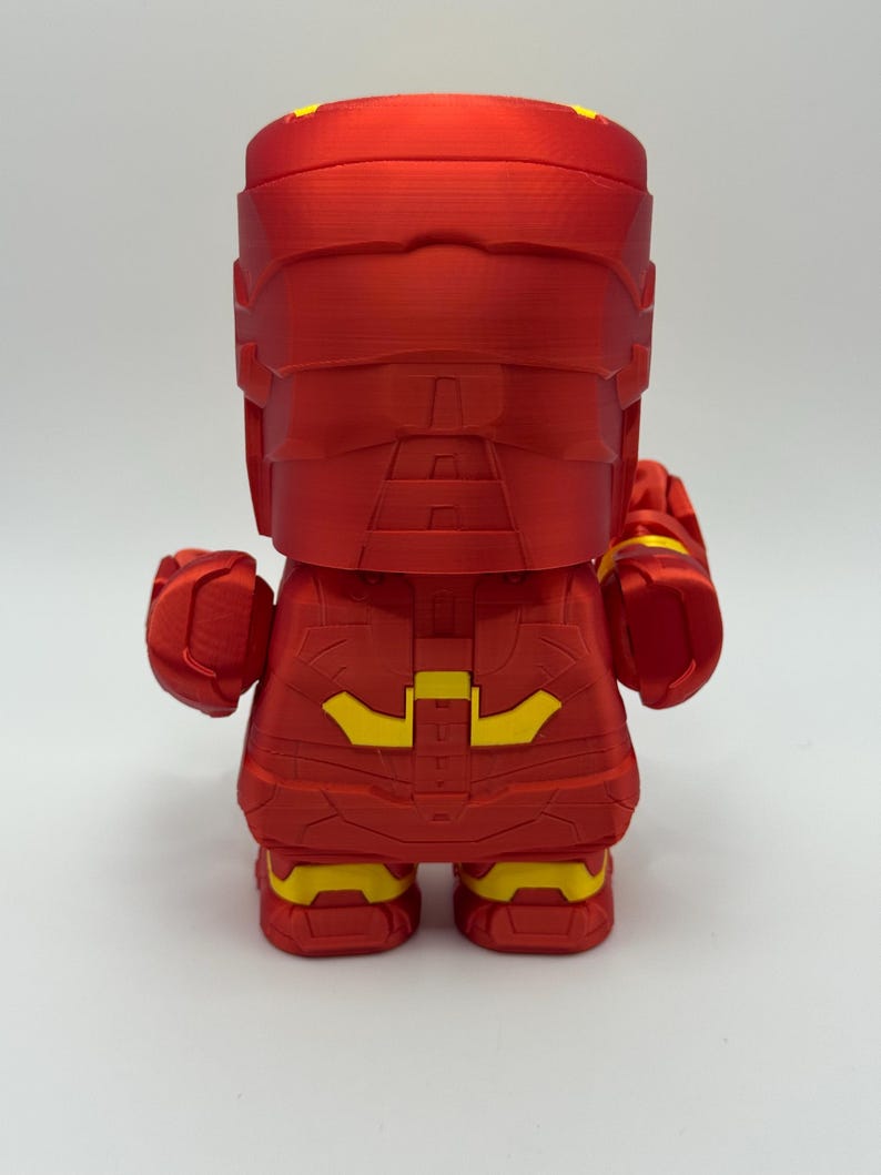 Puede incluir: Figura roja de superh&eacute;roe con detalles amarillos. La figura tiene un dise&ntilde;o en bloques, con casco y traje. Las costuras y texturas son visibles. El dise&ntilde;o sugiere un objeto de colecci&oacute;n o decorativo, posiblemente un personaje de c&oacute;mic.