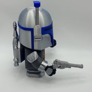 Peut inclure: Figurine argent&eacute;e et bleue repr&eacute;sentant un personnage avec un casque, un jetpack et un pistolet blaster. La figurine a un casque argent&eacute; avec des accents bleus, un corps noir et gris, et un jetpack d&eacute;taill&eacute;. Le pistolet blaster est tenu dans la main droite.
