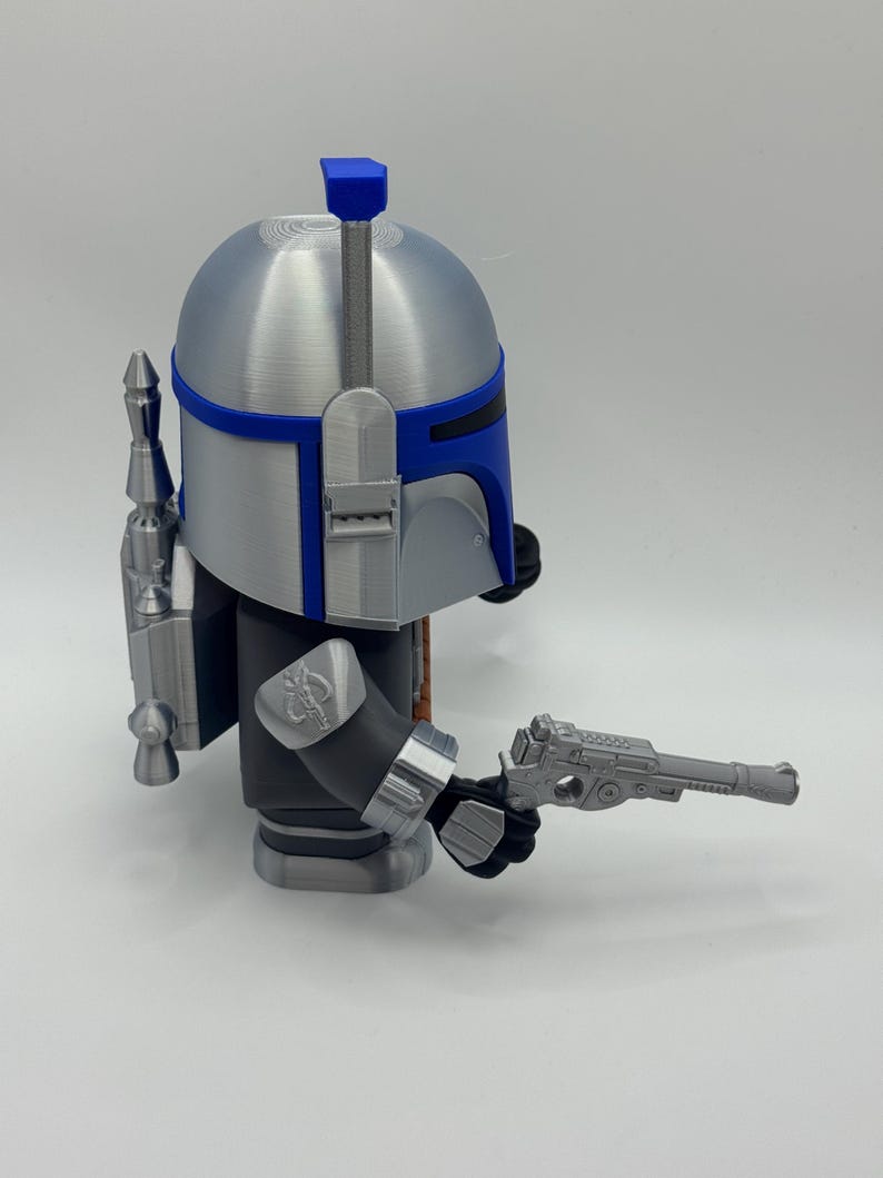 Peut inclure: Figurine argent&eacute;e et bleue repr&eacute;sentant un personnage avec un casque, un jetpack et un pistolet blaster. La figurine a un casque argent&eacute; avec des accents bleus, un corps noir et gris, et un jetpack d&eacute;taill&eacute;. Le pistolet blaster est tenu dans la main droite.