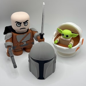 May include: A set of three Star Wars themed figurines. A brown and grey Mandalorian figure with a black lightsaber, a grey Mandalorian helmet, and a green Baby Yoda figure in a white and orange floating pod.