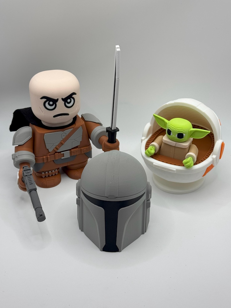 May include: A set of three Star Wars themed figurines. A brown and grey Mandalorian figure with a black lightsaber, a grey Mandalorian helmet, and a green Baby Yoda figure in a white and orange floating pod.