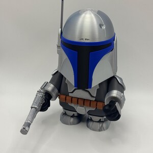 Peut inclure: Figurine stylis&eacute;e d'un personnage d'une franchise de science-fiction. La figurine a un casque argent&eacute; avec des accents bleus, un corps noir et gris et une ceinture marron. Elle tient un pistolet argent&eacute;.