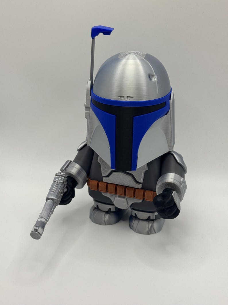 Peut inclure: Figurine stylis&eacute;e d'un personnage d'une franchise de science-fiction. La figurine a un casque argent&eacute; avec des accents bleus, un corps noir et gris et une ceinture marron. Elle tient un pistolet argent&eacute;.