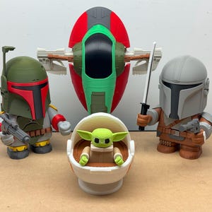 Puede incluir: Colecci&oacute;n de figuras de Star Wars. Incluye una figura de Boba Fett con un bl&aacute;ster, una figura de Mandaloriano con una espada y un bl&aacute;ster, una figura de Grogu en una c&aacute;psula y una nave Slave I.