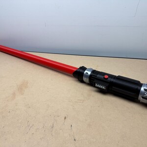 Puede incluir: Un sable de luz rojo con un mango negro con detalles plateados y un bot&oacute;n rojo. El sable de luz mide aproximadamente 102 cm de largo.