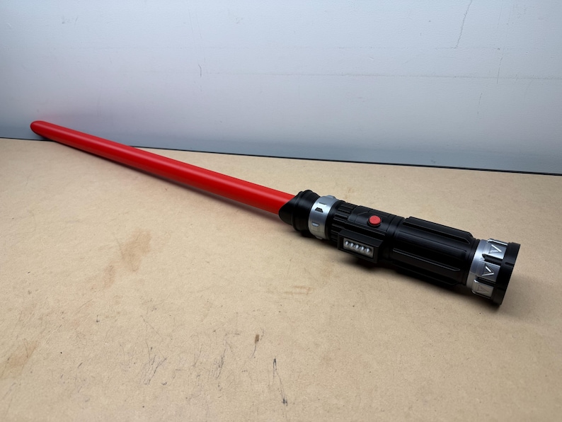 Puede incluir: Un sable de luz rojo con un mango negro con detalles plateados y un bot&oacute;n rojo. El sable de luz mide aproximadamente 102 cm de largo.
