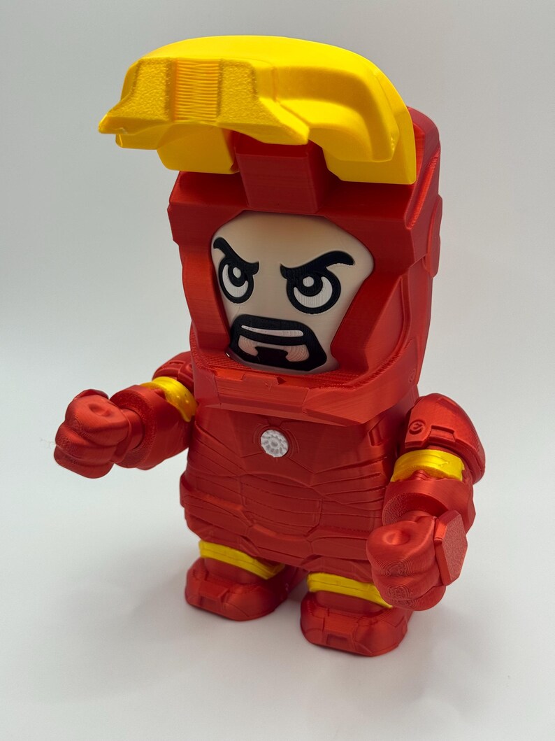 Puede incluir: Una figura de Iron Man roja y amarilla con un dise&ntilde;o en bloques. La figura tiene un casco amarillo y una armadura roja con detalles amarillos. La cara es una versi&oacute;n de dibujos animados de la cara de Iron Man.