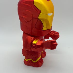 Puede incluir: Figura de Iron Man impresa en 3D en posici&oacute;n de pie. La figura es principalmente roja con detalles dorados en el casco y las articulaciones. El dise&ntilde;o es una representaci&oacute;n estilizada de la armadura del superh&eacute;roe.