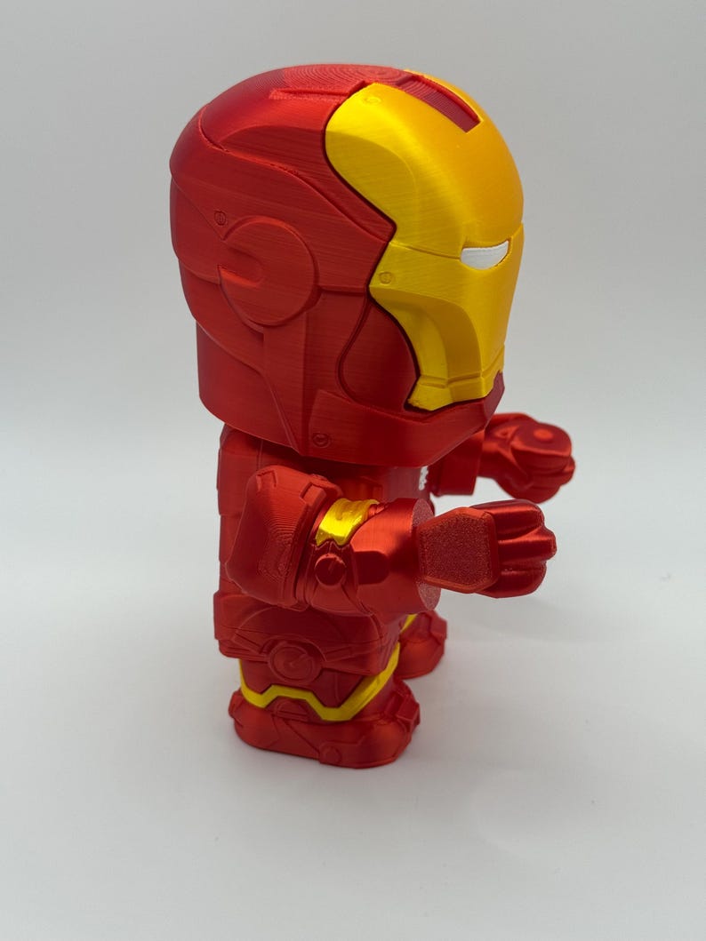 Puede incluir: Figura de Iron Man impresa en 3D en posici&oacute;n de pie. La figura es principalmente roja con detalles dorados en el casco y las articulaciones. El dise&ntilde;o es una representaci&oacute;n estilizada de la armadura del superh&eacute;roe.