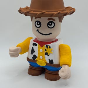 Op de afbeelding: Speelgoedfiguur van een cowboy met een bruine hoed, wit overhemd met zwarte koeienvlekken, rode halsdoek en blauwe broek. De figuur heeft gele mouwen en een sheriff-badge. Een leuk speelgoed.