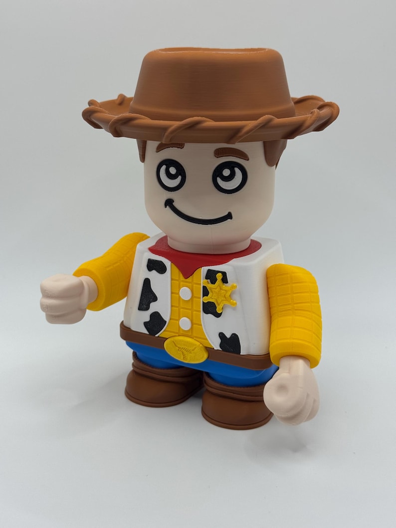 Op de afbeelding: Speelgoedfiguur van een cowboy met een bruine hoed, wit overhemd met zwarte koeienvlekken, rode halsdoek en blauwe broek. De figuur heeft gele mouwen en een sheriff-badge. Een leuk speelgoed.