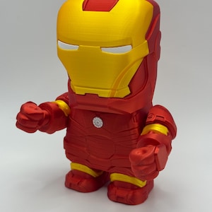 Puede incluir: Una figura de Iron Man roja y dorada con un dise&ntilde;o en bloques. La figura presenta un casco amarillo con ranuras para los ojos blancas, un cuerpo rojo y detalles amarillos en los brazos y las piernas. La figura est&aacute; de pie.