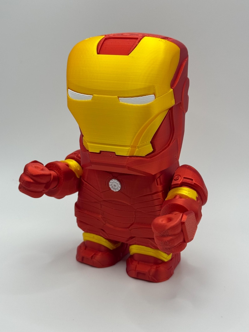 Puede incluir: Una figura de Iron Man roja y dorada con un dise&ntilde;o en bloques. La figura presenta un casco amarillo con ranuras para los ojos blancas, un cuerpo rojo y detalles amarillos en los brazos y las piernas. La figura est&aacute; de pie.