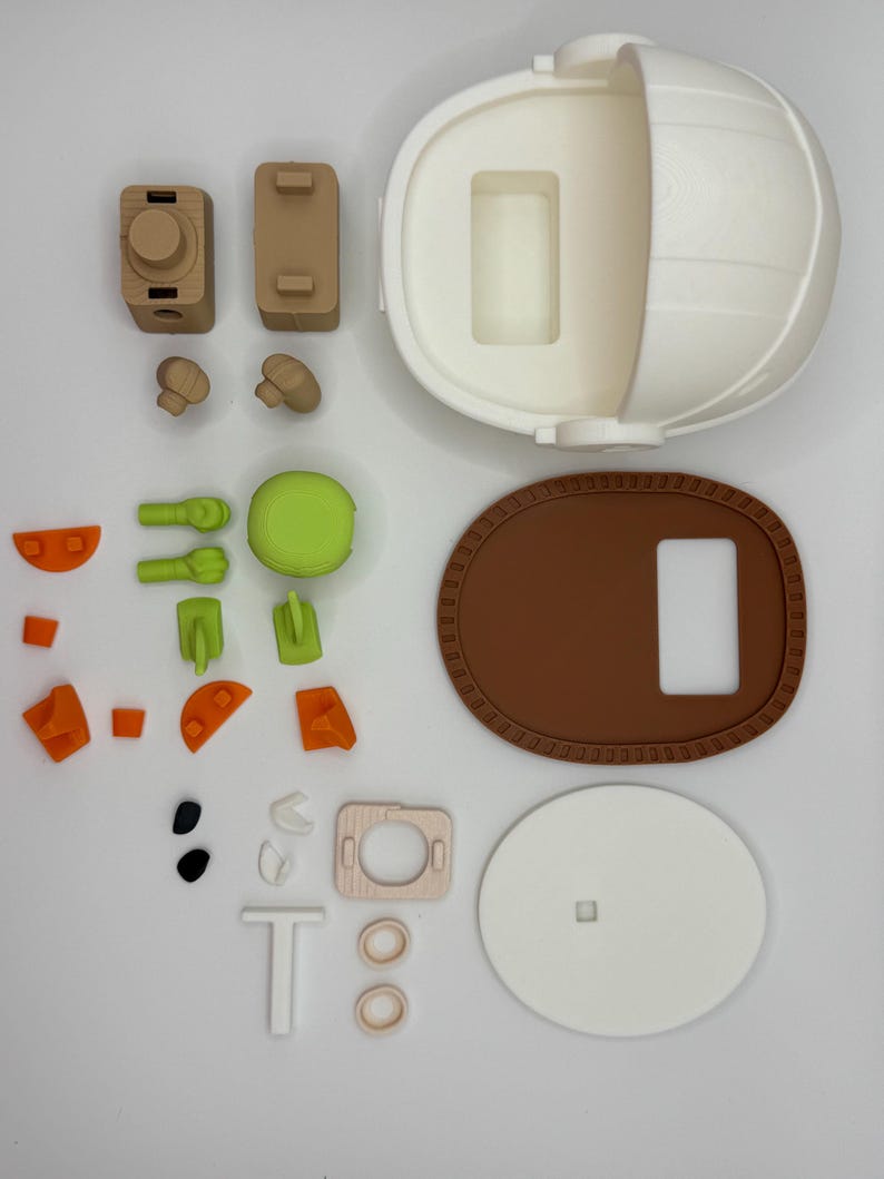 Puede incluir: Un conjunto de juguetes desmontados de varios colores. El conjunto incluye una estructura esf&eacute;rica blanca, una base ovalada marr&oacute;n y piezas m&aacute;s peque&ntilde;as en tonos marr&oacute;n, verde, naranja y blanco. Las piezas parecen estar impresas en 3D, probablemente para un juguete infantil.