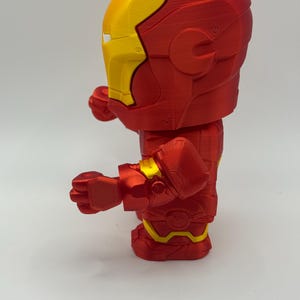 Puede incluir: Una figura de Iron Man roja y amarilla. La figura es una representaci&oacute;n estilizada del superh&eacute;roe, con un cuerpo rojo y detalles amarillos en el casco, las manos y la parte inferior de las piernas. La figura est&aacute; posando con los pu&ntilde;os cerrados.