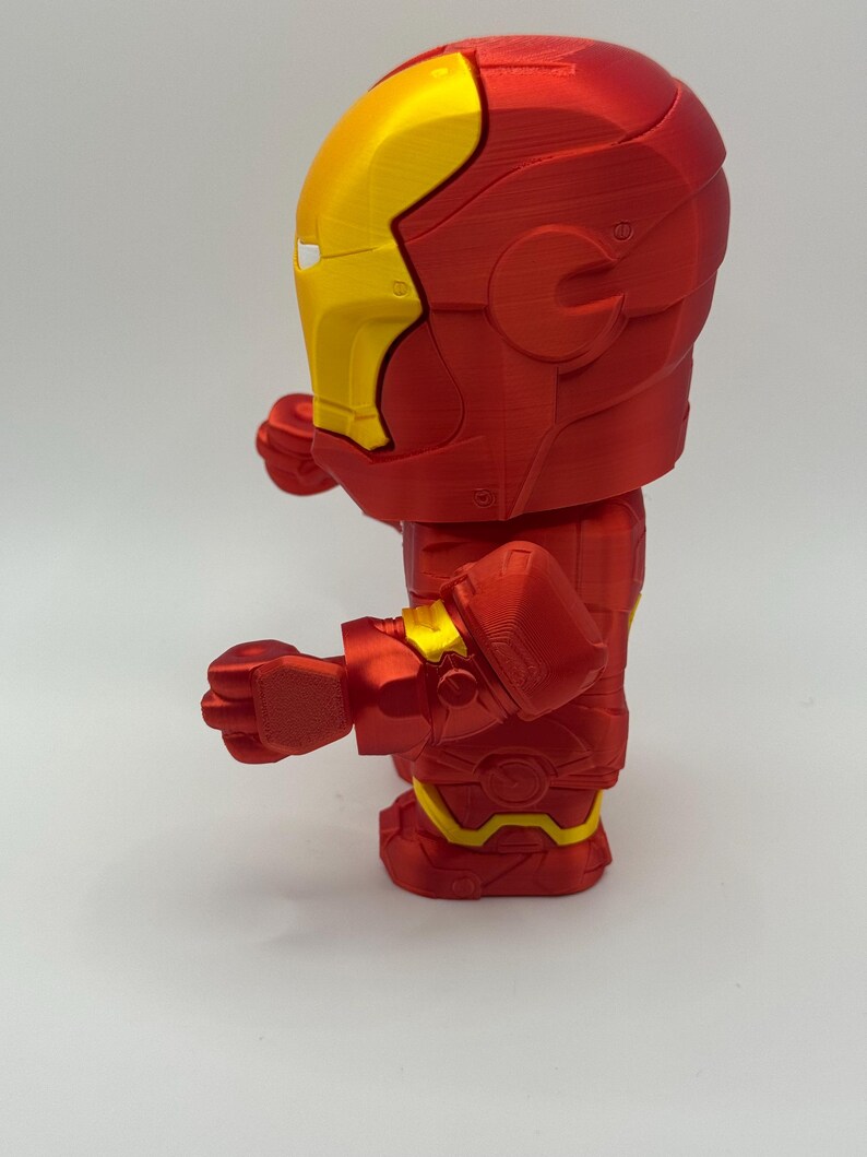 Puede incluir: Una figura de Iron Man roja y amarilla. La figura es una representaci&oacute;n estilizada del superh&eacute;roe, con un cuerpo rojo y detalles amarillos en el casco, las manos y la parte inferior de las piernas. La figura est&aacute; posando con los pu&ntilde;os cerrados.