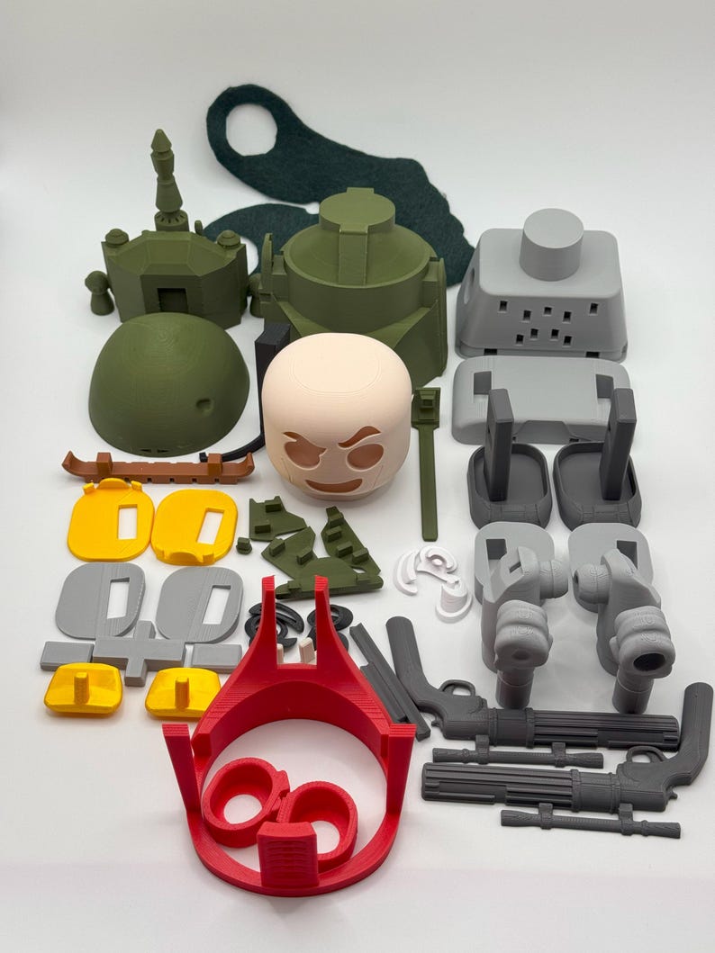 Puede incluir: Un surtido de piezas de juguetes impresas en 3D en varios colores, incluyendo verde oliva, gris, amarillo, rojo y beige. La colecci&oacute;n presenta componentes que se asemejan a un tanque, armas y otros elementos de construcci&oacute;n. Las piezas est&aacute;n dispuestas sobre una superficie blanca.