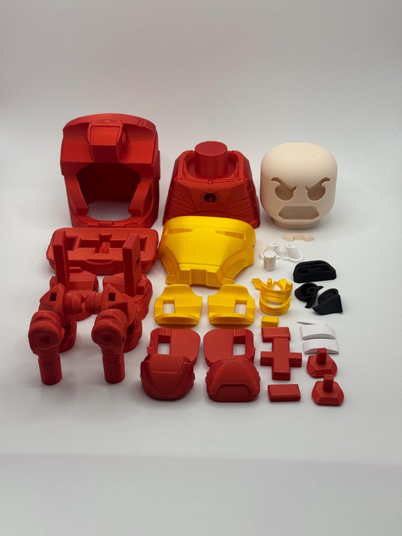 Puede incluir: Un conjunto de componentes de armadura de Iron Man impresos en 3D, en rojo y amarillo. El conjunto incluye un casco, torso, piezas de piernas y una cabeza de expresi&oacute;n neutra. Tambi&eacute;n se incluyen varias piezas m&aacute;s peque&ntilde;as.