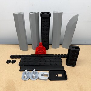May include: A collection of 3D printed components including four grey vertical segments, one grey curved piece, a black textured handle, a red stand, a long black articulated chain, a black rectangular block, and several small grey and black base parts.