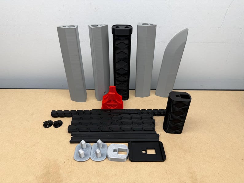 May include: A collection of 3D printed components including four grey vertical segments, one grey curved piece, a black textured handle, a red stand, a long black articulated chain, a black rectangular block, and several small grey and black base parts.