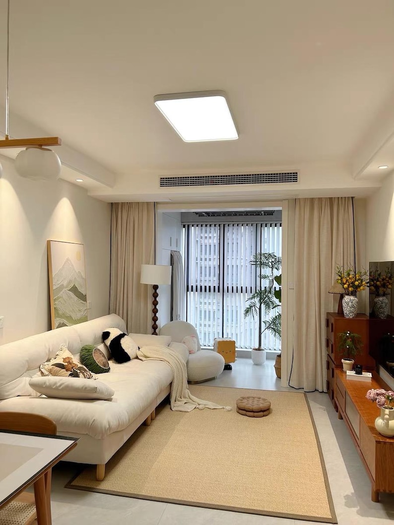 Pu&ograve; includere: Un soggiorno luminoso e arioso con un divano color crema, un tappeto beige e tende chiare. Cuscini decorativi con vari motivi e colori adornano il divano. Un mobile in legno e una lampada da terra completano l'arredamento della stanza. Una grande finestra offre una vista sull'esterno.