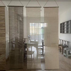 Puede incluir: Cuatro separadores de ambientes colgantes verticales hechos de fibras naturales tejidas en varios tonos de marr&oacute;n, bronceado y crema. Cada panel rectangular est&aacute; suspendido de una varilla de madera delgada en la parte superior e inferior, con texturas distintas.