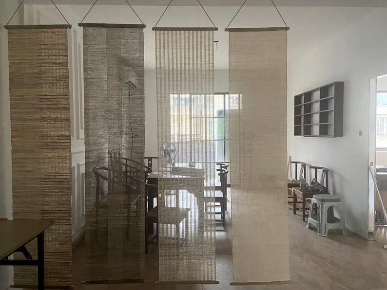 Puede incluir: Cuatro separadores de ambientes colgantes verticales hechos de fibras naturales tejidas en varios tonos de marr&oacute;n, bronceado y crema. Cada panel rectangular est&aacute; suspendido de una varilla de madera delgada en la parte superior e inferior, con texturas distintas.