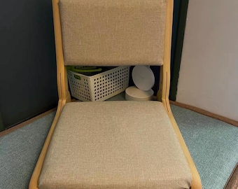 May include: A beige upholstered floor chair with a light wood frame. The chair has a rectangular seat and backrest, and the frame is curved. The chair is designed for sitting on the floor.