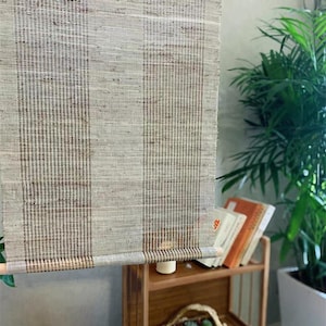 Puede incluir: Un tapiz rectangular de tela tejida con un patr&oacute;n de rayas verticales en tonos beige, arena y marr&oacute;n oscuro. El tejido presenta una textura de cuadr&iacute;cula visible y est&aacute; suspendido de una varilla de madera delgada en la parte superior e inferior.