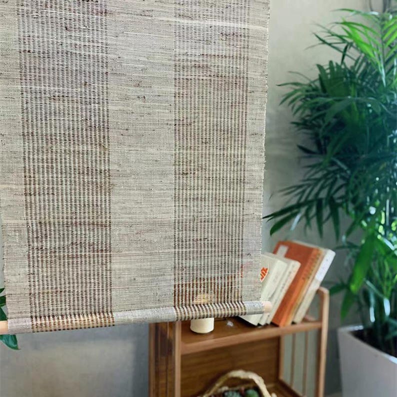 Puede incluir: Un tapiz rectangular de tela tejida con un patr&oacute;n de rayas verticales en tonos beige, arena y marr&oacute;n oscuro. El tejido presenta una textura de cuadr&iacute;cula visible y est&aacute; suspendido de una varilla de madera delgada en la parte superior e inferior.