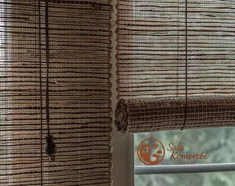 Puede incluir: Primer plano de dos persianas enrollables de bambú tejido. Las persianas son una mezcla de marrón y beige, con un patrón de rayas horizontales. Una persiana está enrollada y la otra está bajada. Un cordón cuelga de la persiana bajada.