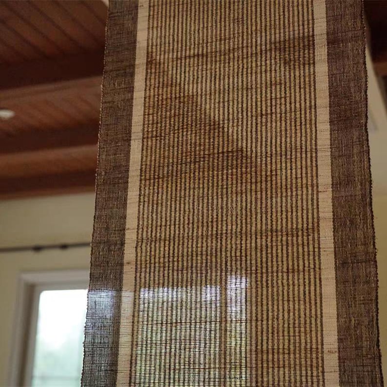 Puede incluir: Un camino de mesa rectangular con textura tejida, que presenta un panel central de rayas verticales de color beige claro flanqueado por dos bordes anchos de color marr&oacute;n oscuro a cada lado. La tela tiene un patr&oacute;n de tejido grueso visible.