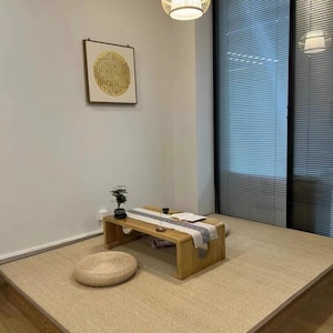Pu&ograve; includere: Una stanza minimalista in stile giapponese con un tavolino basso in legno, un runner decorativo e un cuscino rotondo intrecciato. La stanza ha un pavimento in tatami e un'opera d'arte incorniciata.