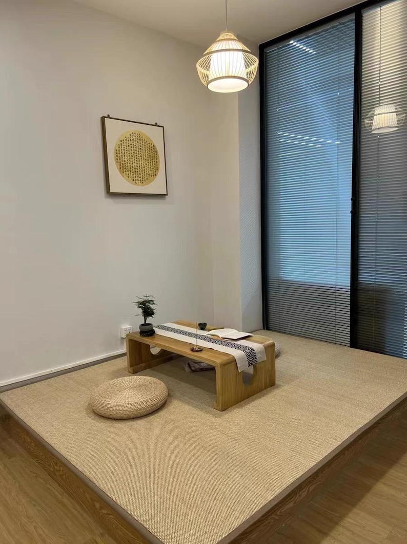 Pu&ograve; includere: Una stanza minimalista in stile giapponese con un tavolino basso in legno, un runner decorativo e un cuscino rotondo intrecciato. La stanza ha un pavimento in tatami e un'opera d'arte incorniciata.