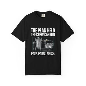 Könnte beinhalten: Ein schwarzes T-Shirt mit einer Grafik eines silbernen industriellen Druckbehälters und Luftschlauchsystems vor einem blauen Rasterhintergrund. Der Text THE PLAN HELD THE CREW CARRIED PREP. PRIME. FINISH. steht in weißen Großbuchstaben.