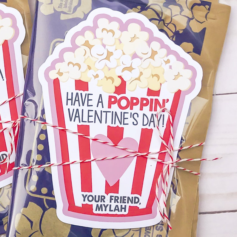 May include: A white and pink popcorn box with red stripes and a pink heart. The box has the text "Have a Poppin' Valentine's Day!" and "Your Friend, Mylah".
